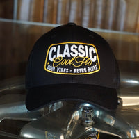 Coo Flo black trucker cap with embroidered yellow and white 'Classic, cool vibes, retro rides' design.