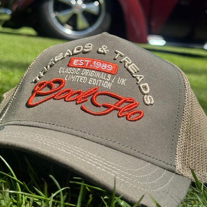 Cool Flo Threads and Treads design cap placed on grass on a sunny day with a Volkswagen Beetle in the background. The olive and khaki cap features complimentary orange and khaki embroidery.
