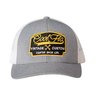 Cool Flo Vintage Custom. Grey and white trucker cap with embroidered yellow, black and white badge with cross-spanners. Carter Bros. London.