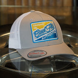 Cool Flo Authentic Cruising Co - Trucker cap with silver/grey front and white mesh a with a yellow, white, silver and turquoise embroidered badge design