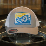 Cool Flo Authentic Cruising Co - Trucker cap with silver/grey front and white mesh a with a yellow, white, silver and turquoise embroidered badge design