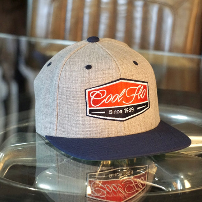 Cool Flo Badge two-tone snapback cap in grey and navy. Embroidered with a red, navy and white badge design.