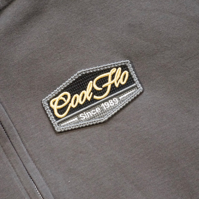 Close-up of the Charcoal zip hoody with Cool Flo Since 1989 3D puff embroidered badge in grey, black, white and golden yellow.