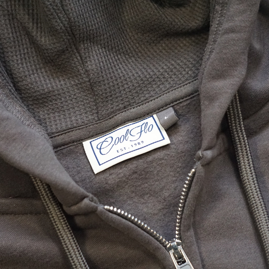 Close-up of neck label, zip and hood detail of the Charcoal zip hoody with Cool Flo Since 1989 3D puff embroidered badge in grey, black, white and golden yellow..