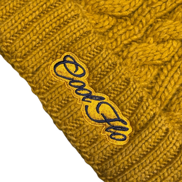 Close-up of Cool Flo Cable Knit Bobble Hat in Mustard with mustard and navy Cool Flo embroidered logo on the cuff.
