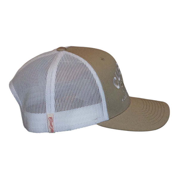 A khaki custom trucker hat with white mesh side panels. The front features white embroidered text reading 'CUSTOM' with 'Cool Flo' in cursive underneath and 'CUSTOM EDITION' with star accents.  The side view features an off-white Cool Flo loop tag with red script logo. 
