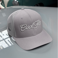 Front view of a Cool Flo silver-grey trucker cap featuring a raised 3D embroidered Script logo in tonal silver-grey and a curved visor.  Positioned on the bonnet of a grey classic car.