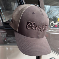 A brown and khaki trucker cap featuring the 'Cool Flo' script logo embroidered in brown across the front, displayed against a Cool Flo classic vehicle.