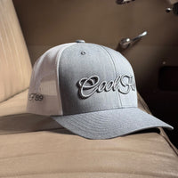 A heather grey trucker cap with white mesh side panels, and 'Cool Flo' embroidered in grey script across the front.