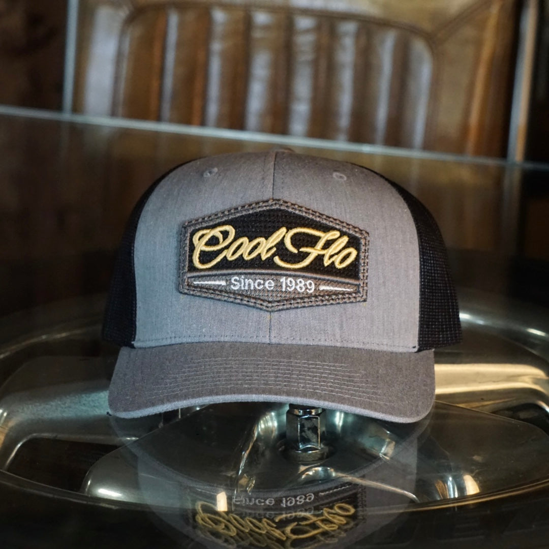 Grey and black trucker cap with Cool Flo Since 1989 puff-embroidered badge sewn onto front.