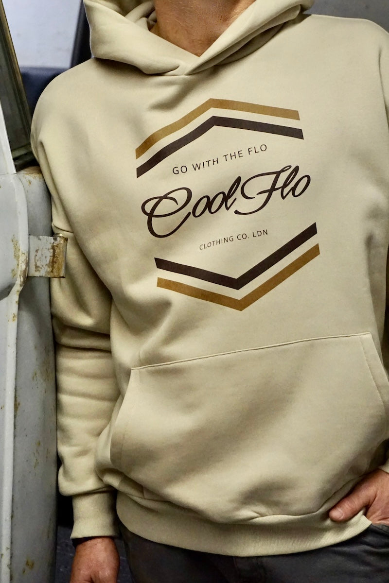 Cropped image of model wearing a stone colour hoody with light and dark brown chevron Cool Flo Go With the Flo printed design, stood by a vintage grey VW bus.