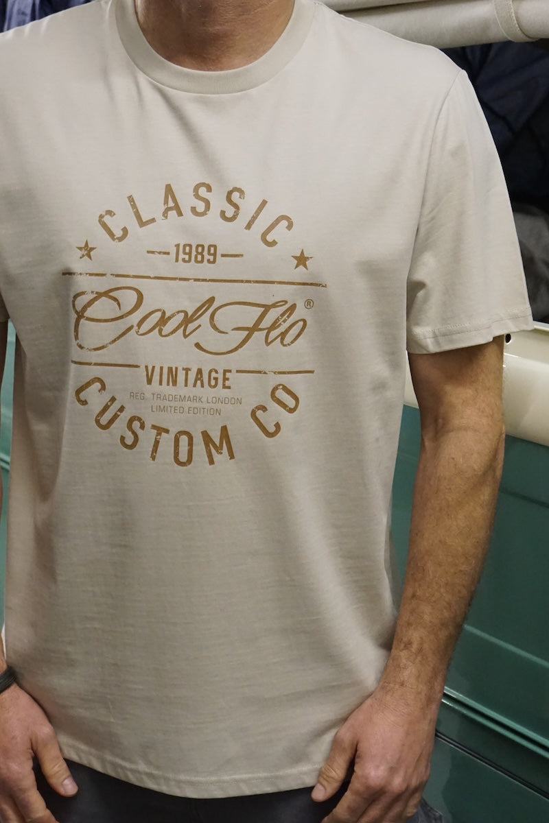Close-up of model standing by a vintage cream and green VW pick-up truck, wearing a stone colour Cool Flo t-shirt with 'Classic Cool Flo Vintage Custom Co' text design printed in brown on the chest.