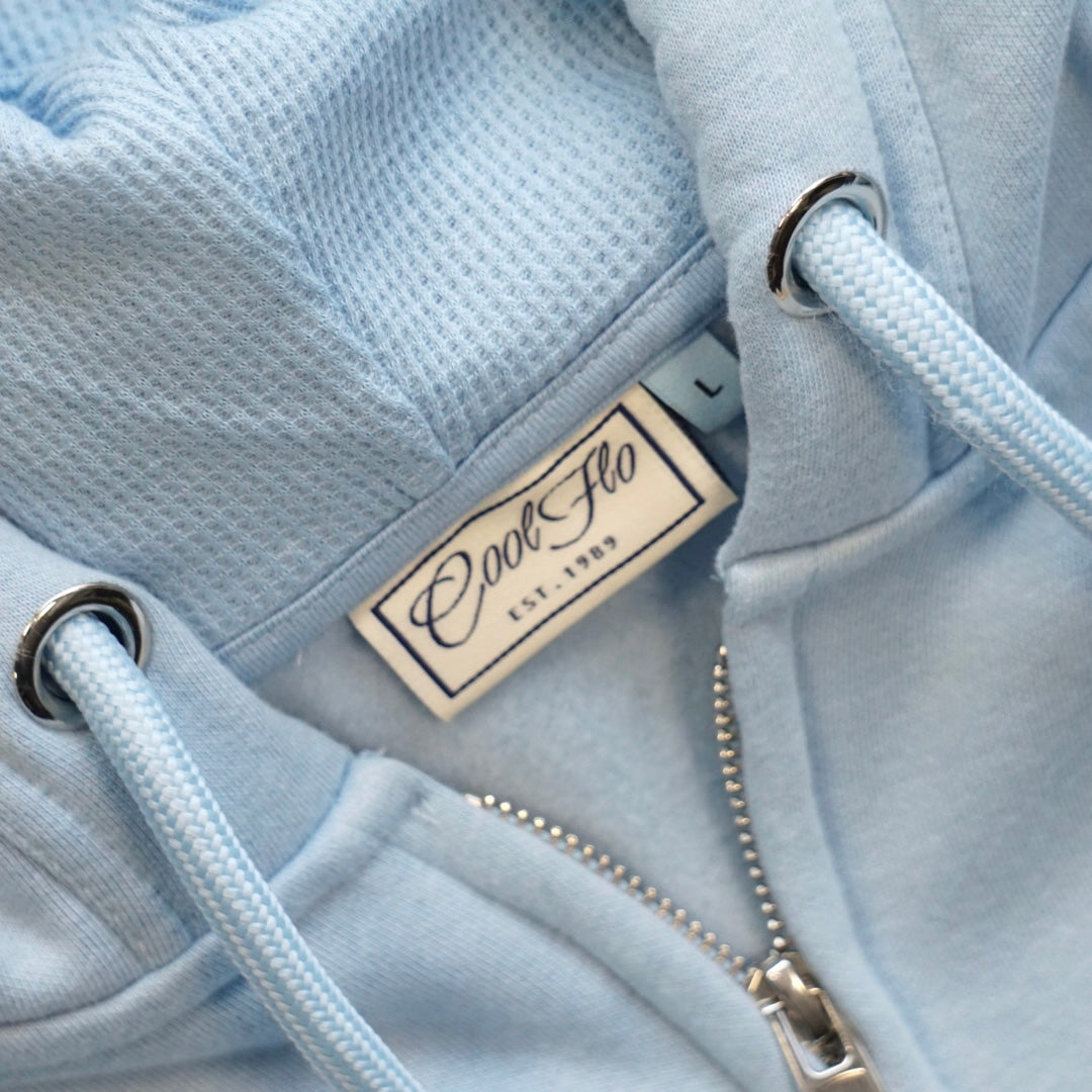 Close-up of neck label and hood pulls of light blue zip hoody with a navy Cool Flo script logo embroidery.