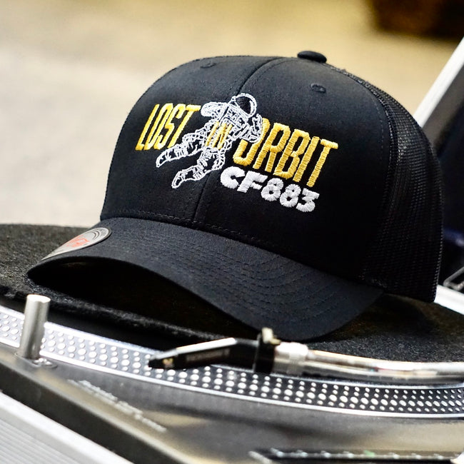 Lost In Orbit CF883 embroidered black trucker cap with Cool Flo silver peak sticker sitting on record deck