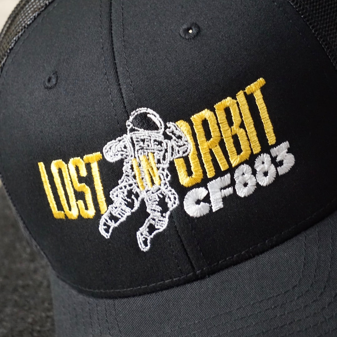 Lost In Orbit CF883 embroidered black trucker cap with Cool Flo silver peak sticker sitting on record deck