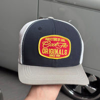 Front view of a Cool Flo Originals trucker cap in Blue/White/Grey featuring an embroidered Originals badge in Red, Yellow and White and a curved visor