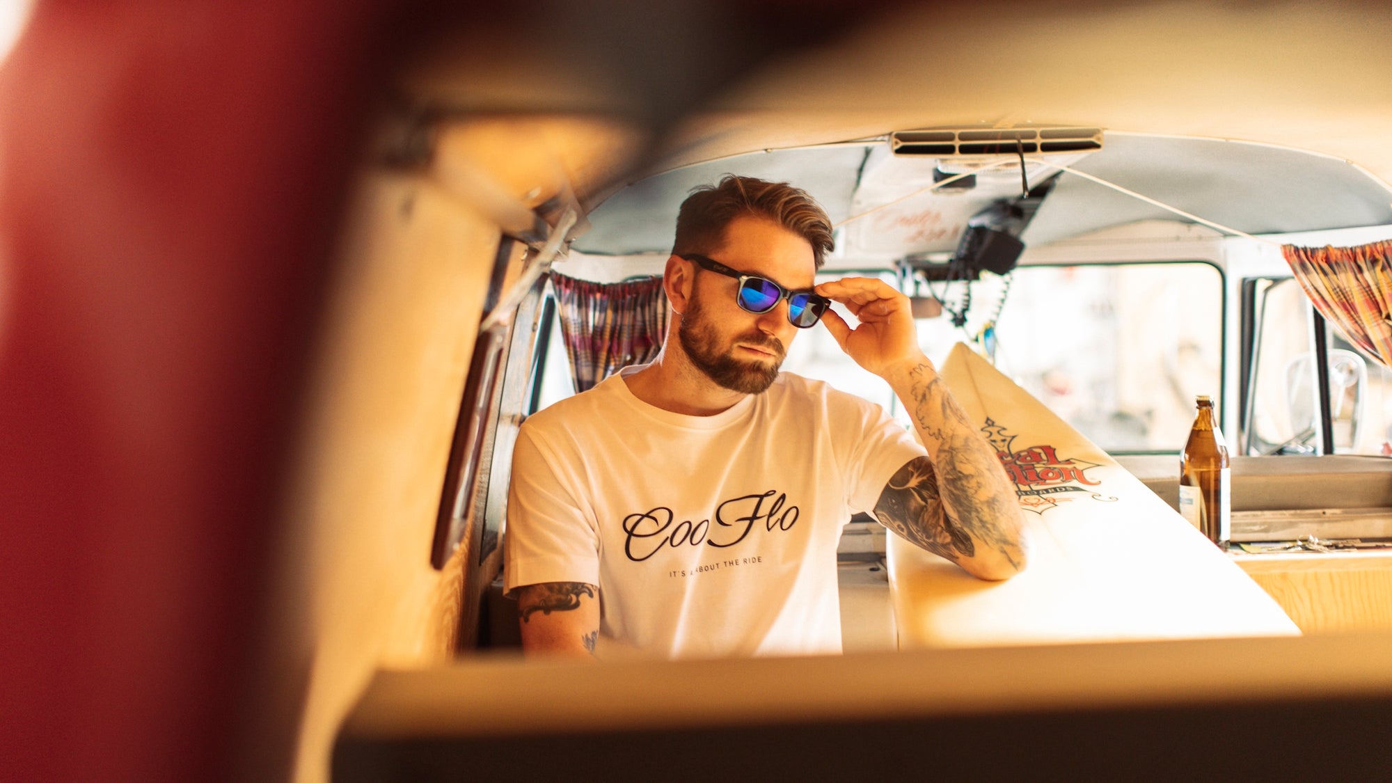 Male model wearing blue and black Cool Flo sunglasses and a Cool Flo logo white t-shirt inside a vintage splitscreen VW campervan.