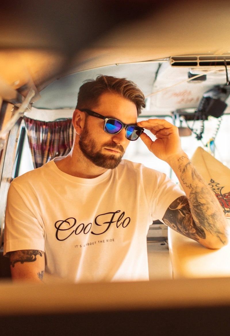Male model wearing blue and black Cool Flo sunglasses and a Cool Flo logo white t-shirt inside a vintage splitscreen VW campervan.