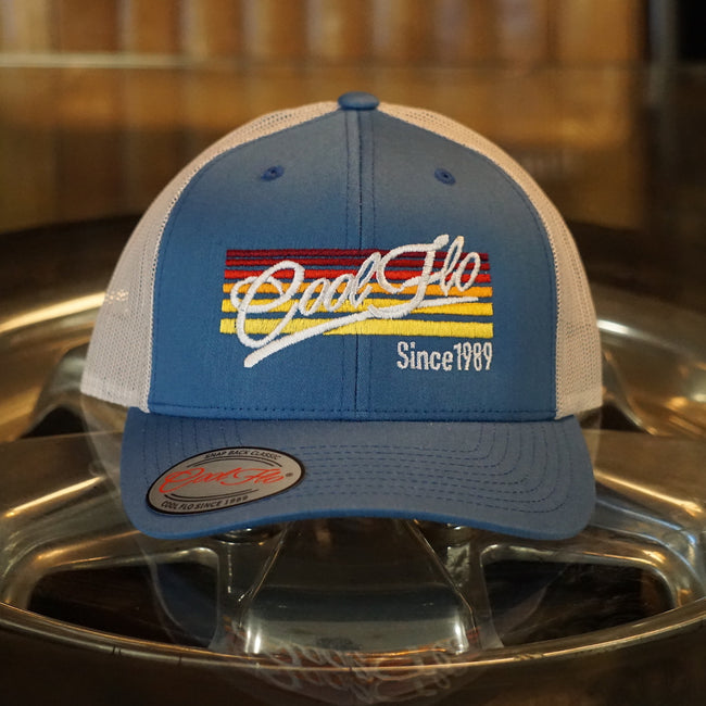 Cool Flo Sunlines trucker cap with a blue front and silver grey mesh. Cool Flo logo and Since 1989 embroidered against a background of graduating lines in sunset colours.
