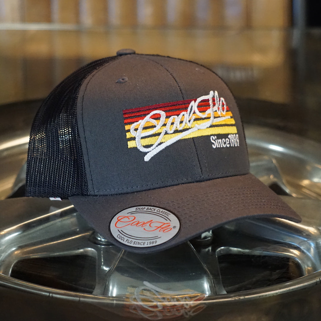 Cool Flo Sunlines dark grey trucker cap with the Cool Flo logo and Since 1989 embroidered against a background of graduating lines in sunset colours.