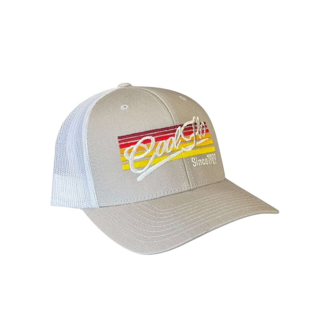 Cool Flo Sunlines trucker cap with a silver grey front and white mesh. Cool Flo logo and Since 1989 embroidered against a background of graduating lines in sunset colours. (Side view.)