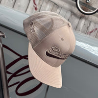 Cool Flo Khaki trucker cap with a raised 3D embroidered Cool Flo Swoosh logo in brown.  Set against a backdrop featuring a light grey Cool Flo classic vehicle.