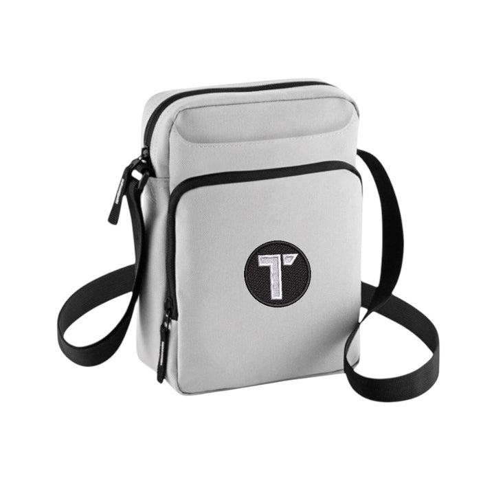 Tenacious light grey cross-body bag with an embroidered black and white 'T' logo on the front.