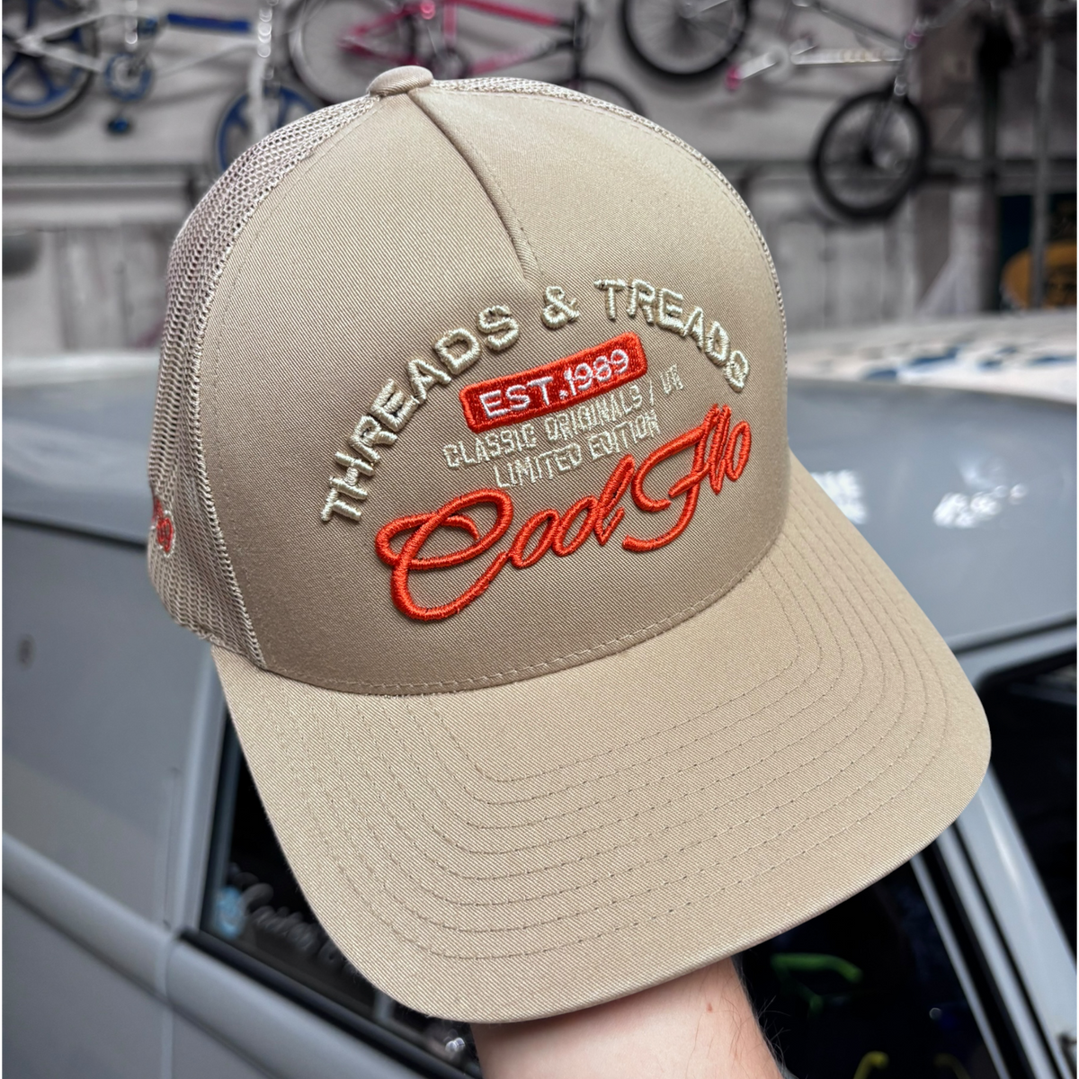 Front view of a Cool Flo Threads & Treads trucker cap in Khaki featuring embroidered Threads & Treads artwork with a structured front panel and curved visor