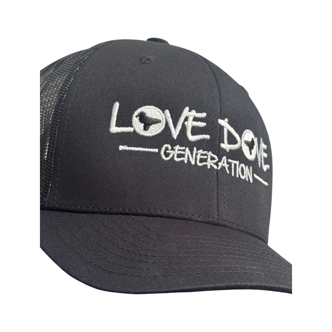 Black trucker cap with embroidered white 'Love Dove Generation' on the front_close up of embroidered logo - close up of logo_side view.