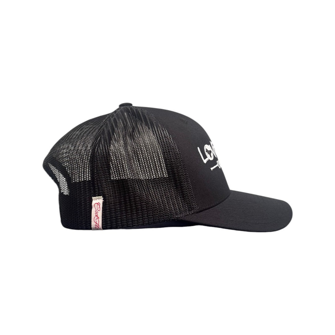Black trucker cap with embroidered white 'Love Dove Generation' on the front_close up of embroidered logo - side view.