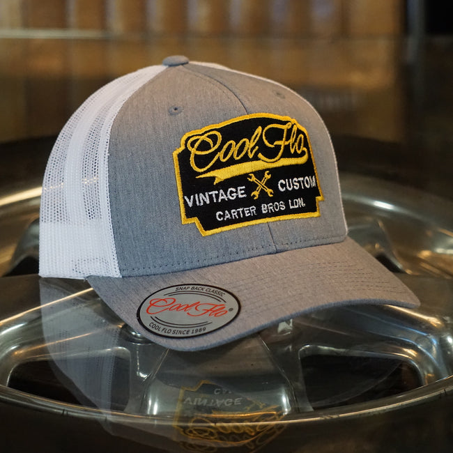 Cool Flo Vintage Custom. Grey and white trucker cap with embroidered yellow, black and white badge with cross-spanners. Carter Bros. London.
